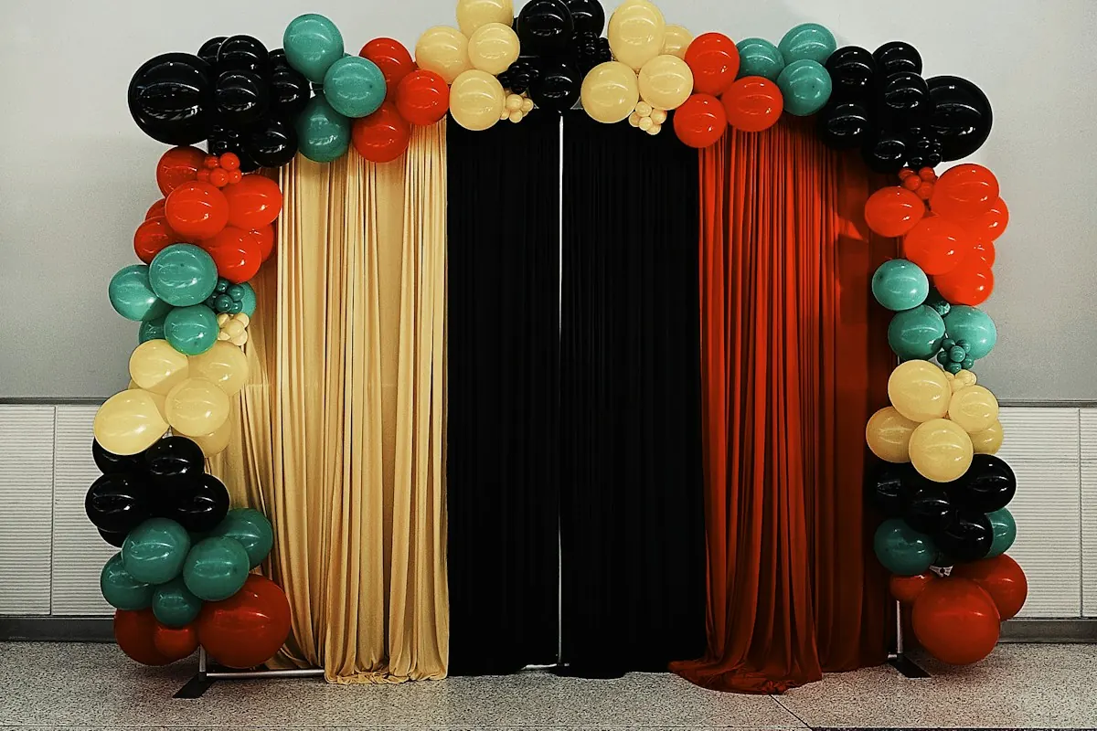 Black, orange and gold balloon arch framing black, gold and orange curtains, an example of a launch or event backdrop