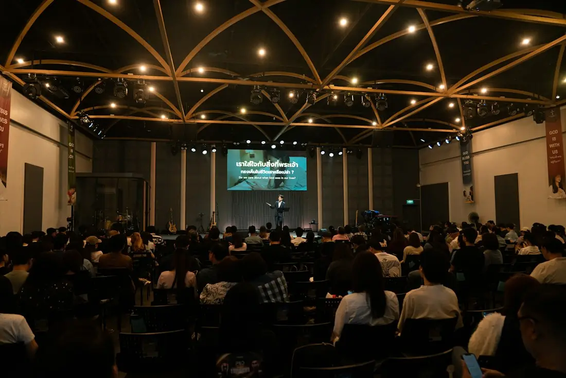 Conference hall with a speaker on a lit stage in front of a seated audience