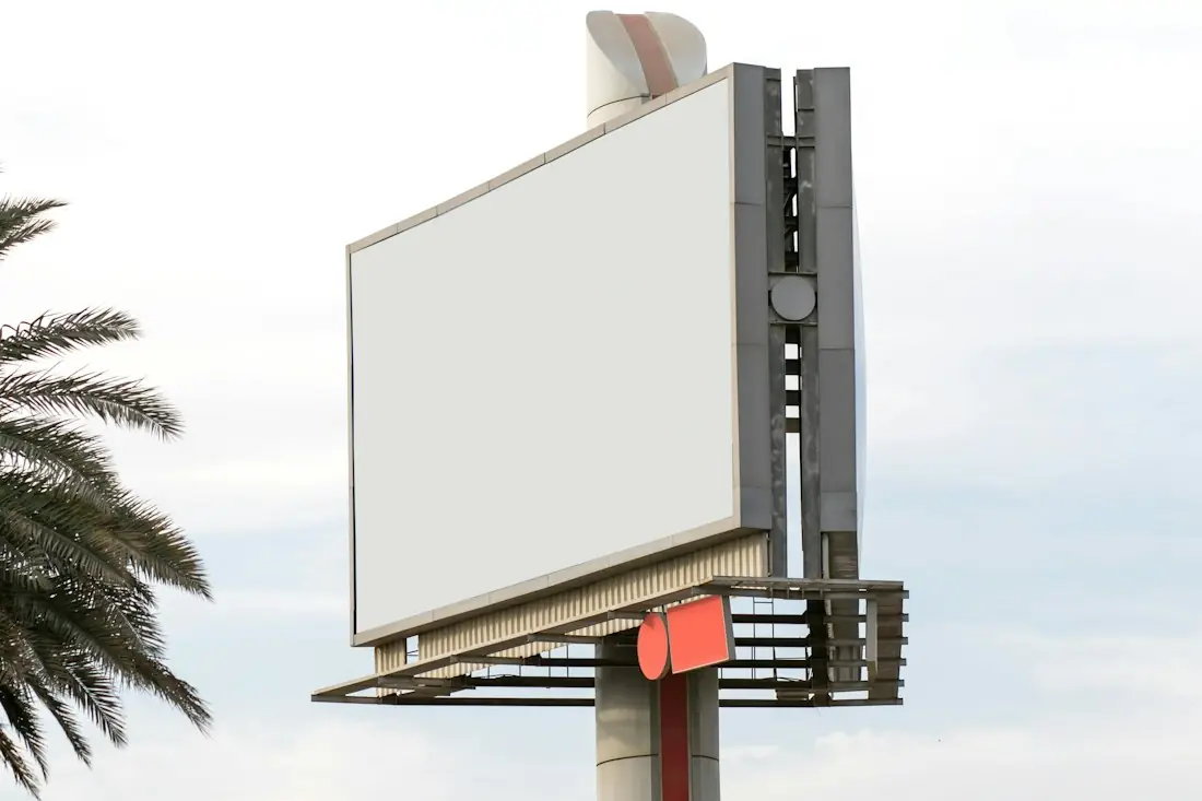 Blank roadside billboard on a steel frame beside a palm tree