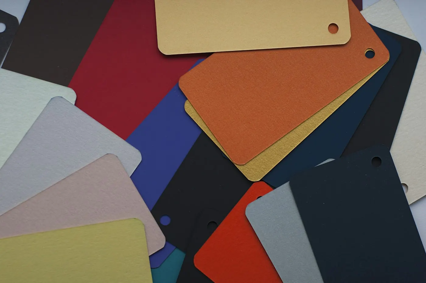 Pile of coloured material sample tags in different finishes, used to compare signage material and colour options