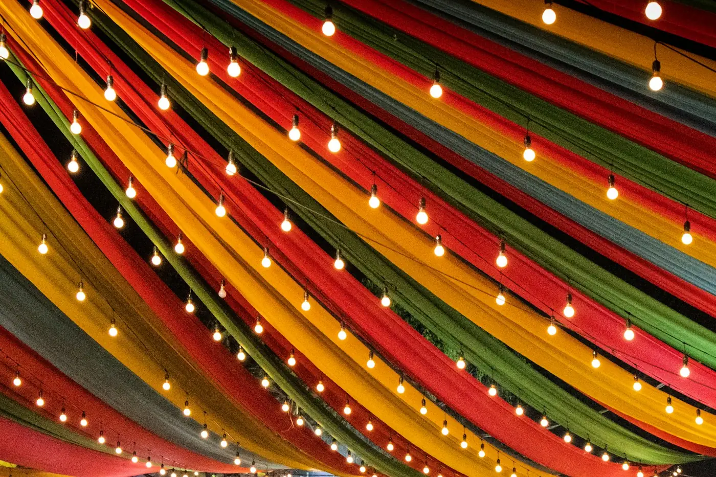 Colourful draped fabric canopy hung with string lights at an outdoor event