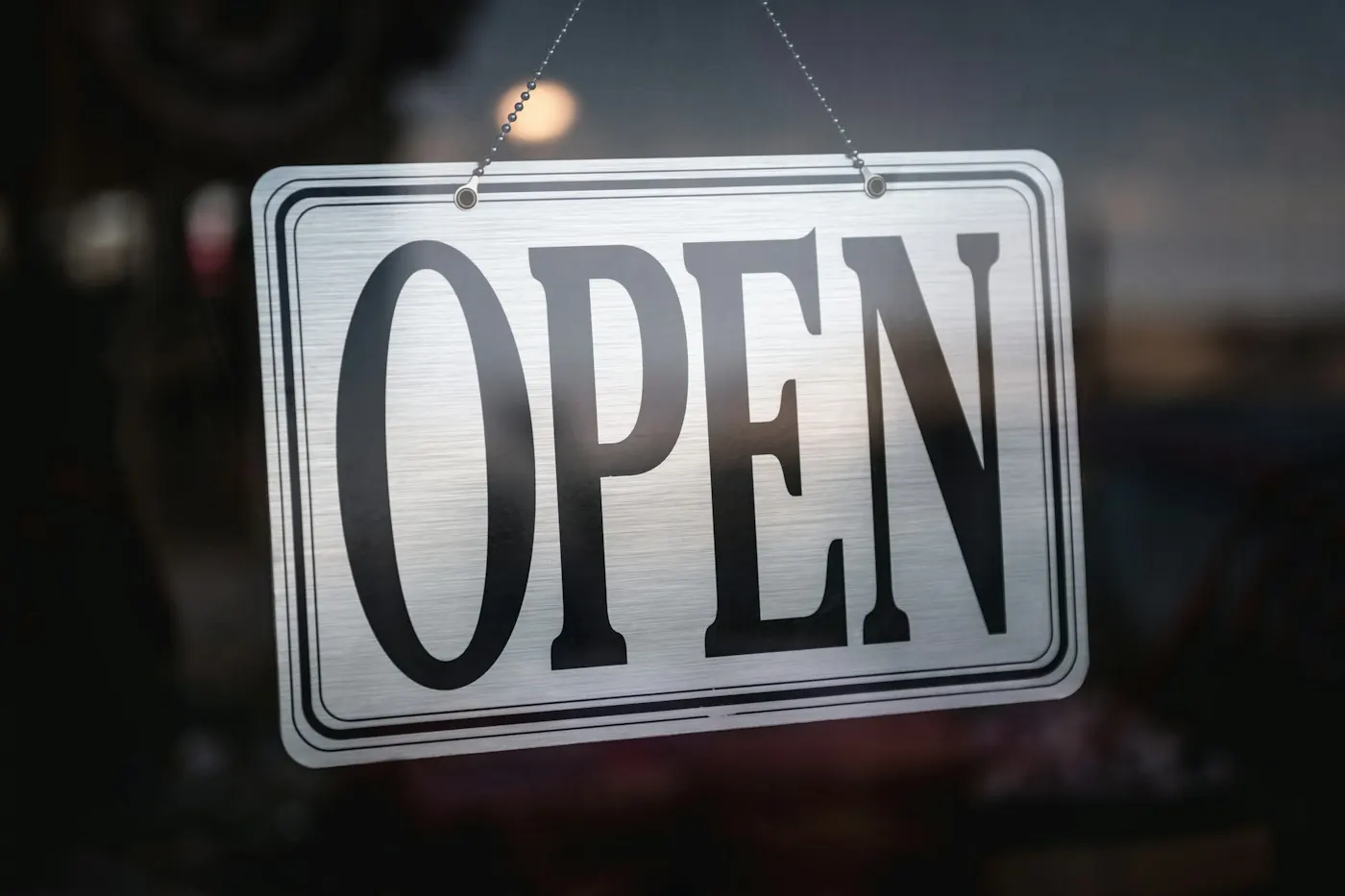 Metal open sign hanging on a glass shop door, a first step when launching a new business
