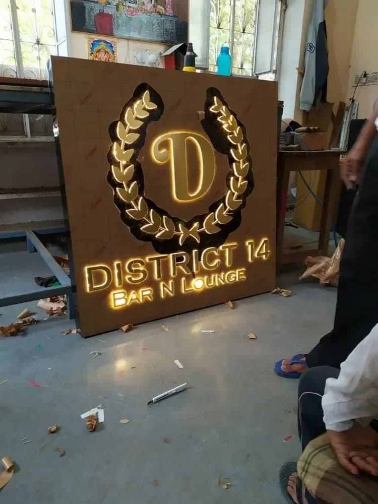 Wooden signboard with a lit gold emblem and lettering, photographed during fabrication, signage work by iMad, Jaipur